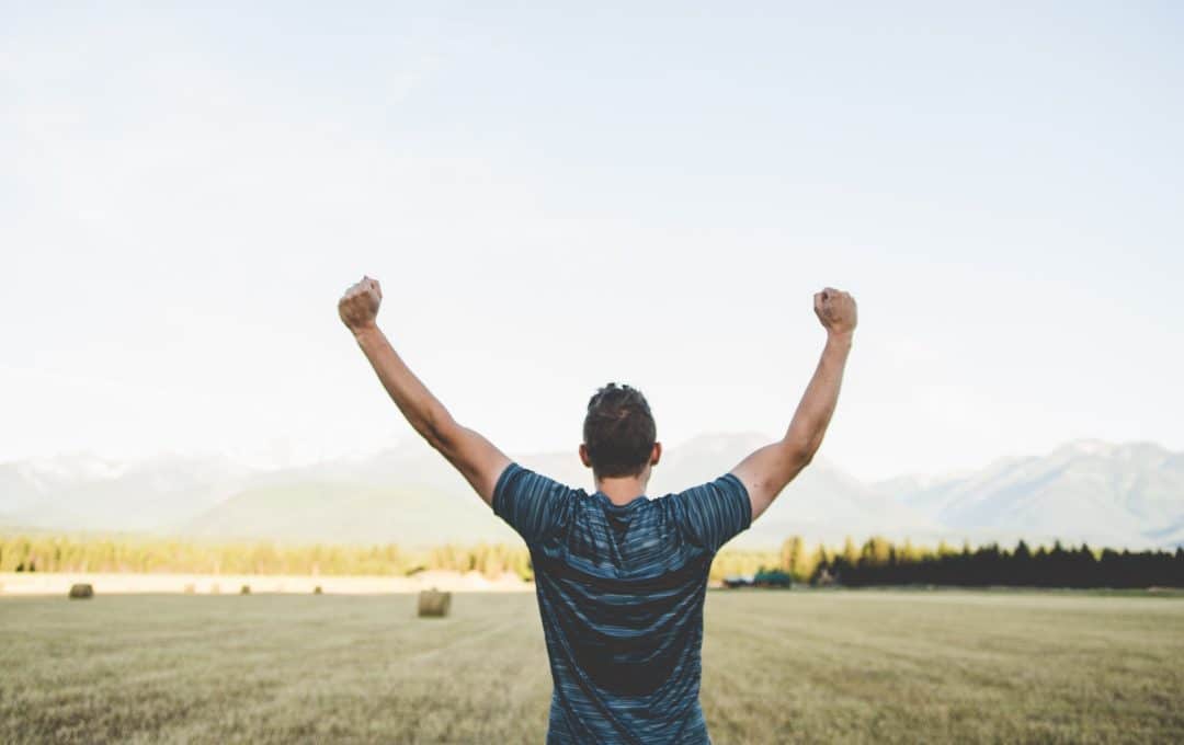 A person celebrating a success by raising their arms in an open field.