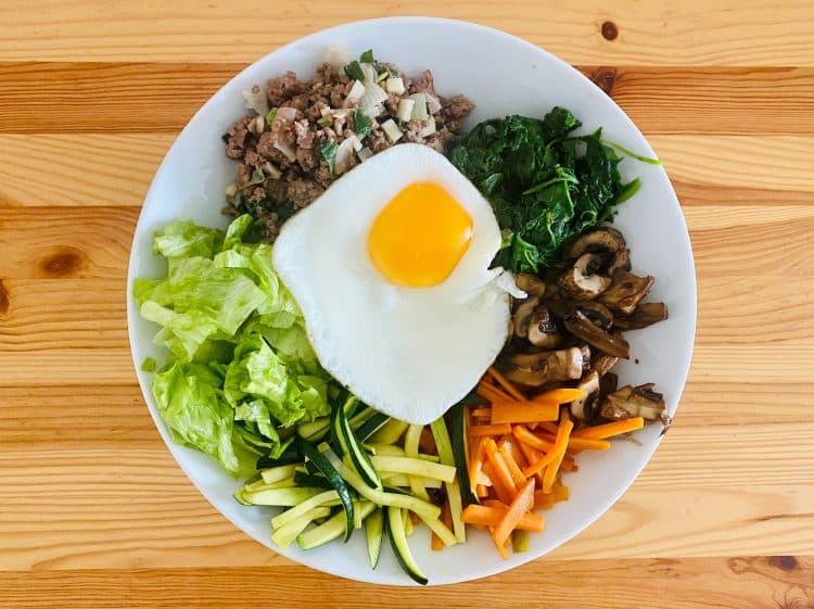 A topdown view of a plate of vegetables, chopped meat, and an egg on top.