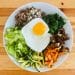 A topdown view of a plate of vegetables, chopped meat, and an egg on top.