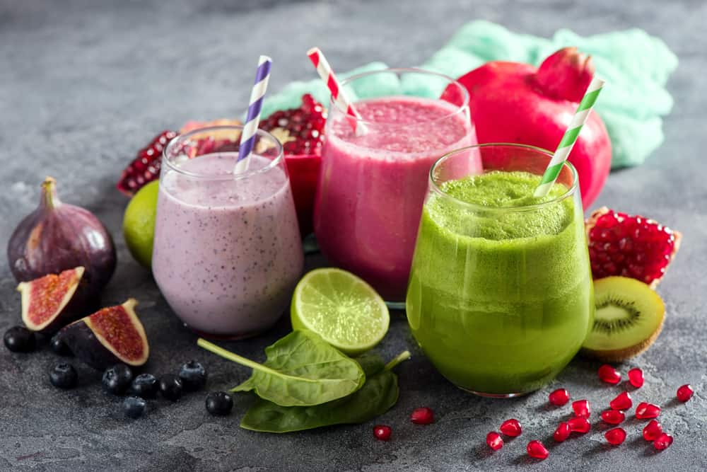 A closeup of some smoothies in glasses with straws.