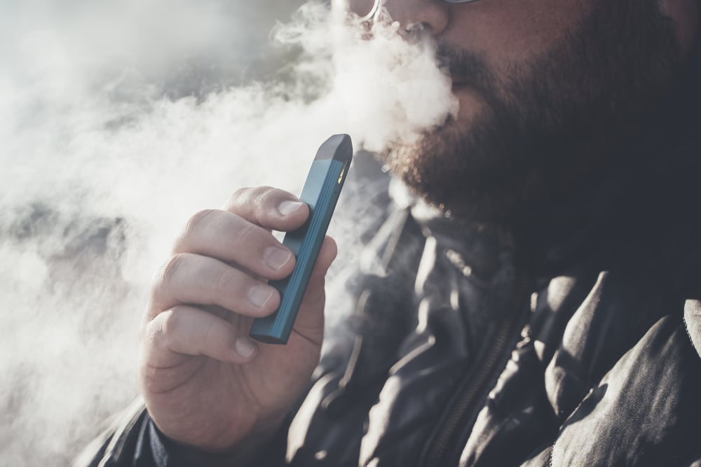 A man blowing out smoke while holding a vape.