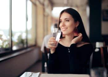 A woman sitting inside and about to drink a glass of water.