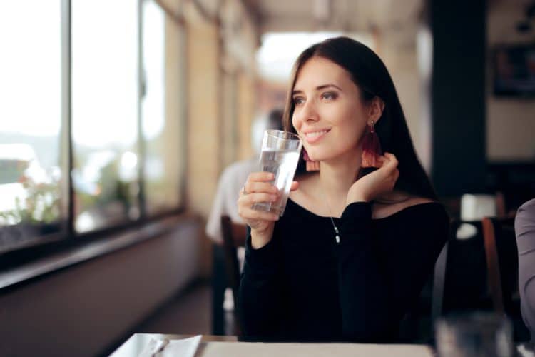 A woman sitting inside and about to drink a glass of water.