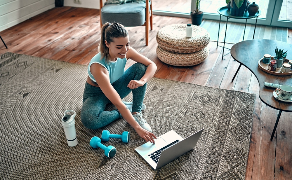 A woman sitting in the middle of a room smiling and doing something on her laptop.