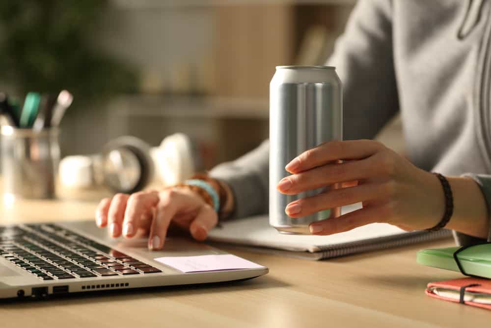 A closeup of a gray can in someone's hand who's working on their laptop.