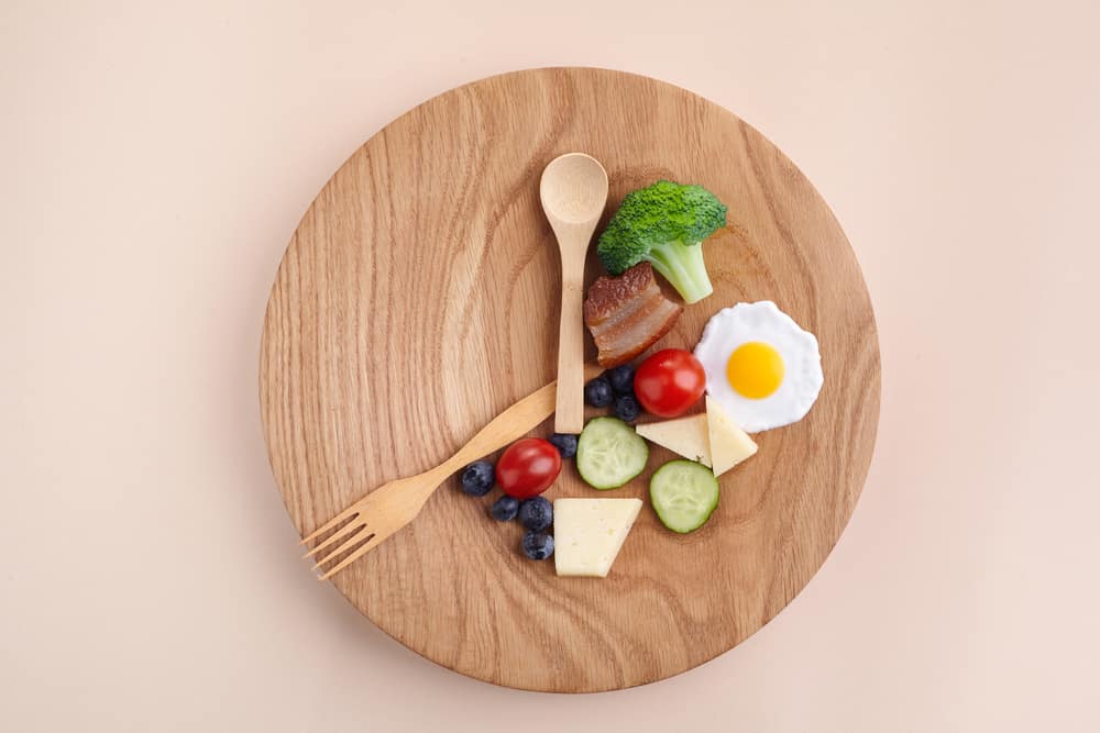 An overhead shot of a wooden plate with a fork, spoon, and some food, all laid out like a clock.
