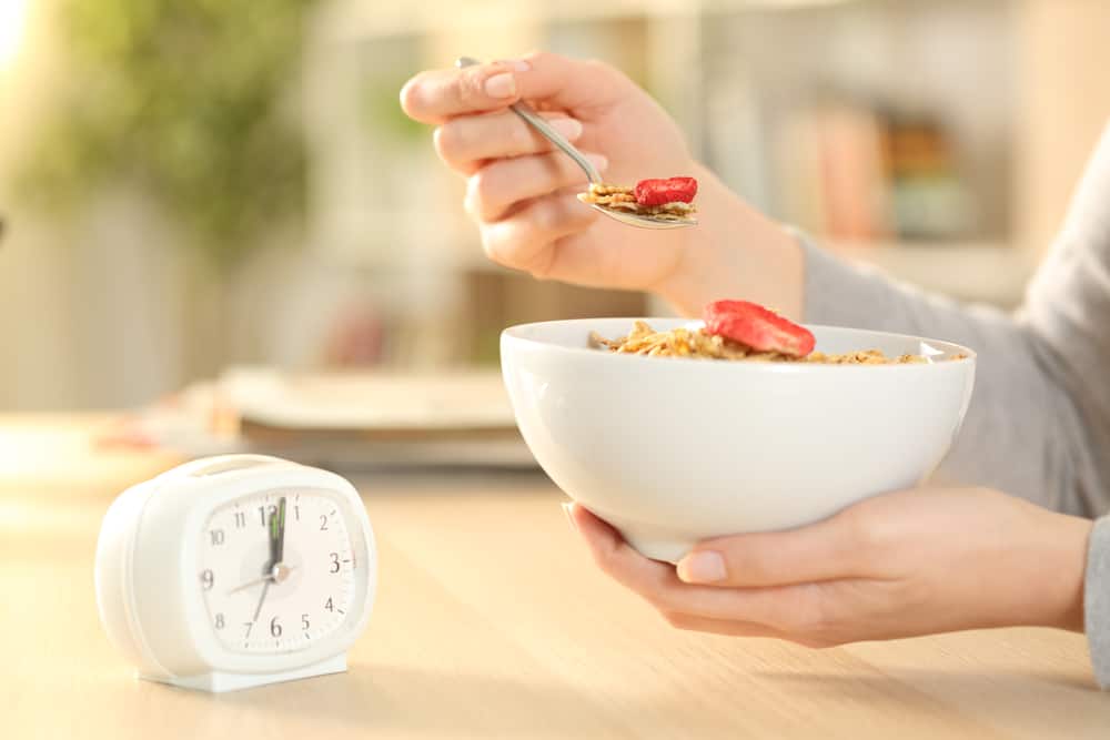 Person eating a bowl of cereal and fruit with a timer nearby.