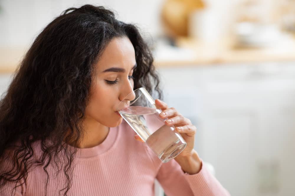 A woman drinking water from a tall glass.