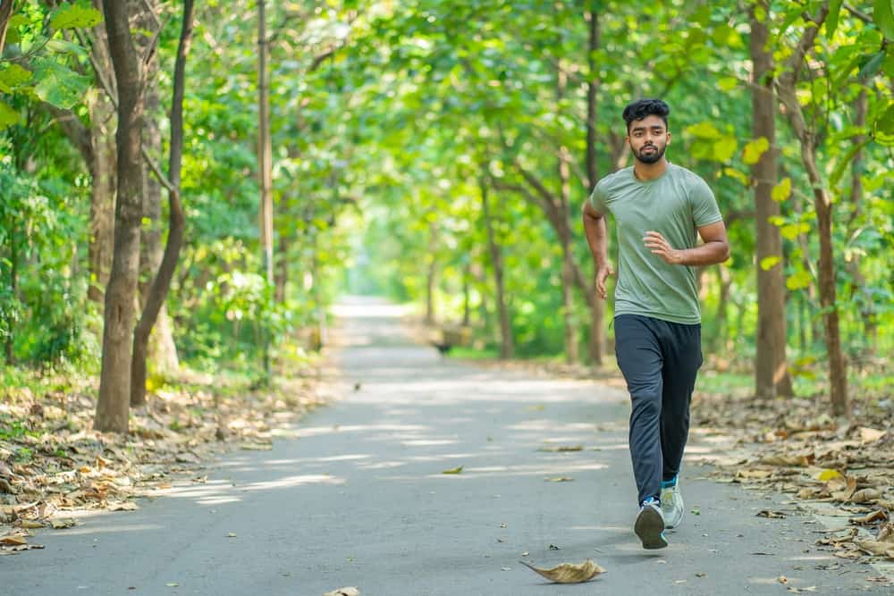 A man power walking on a path through a forest.