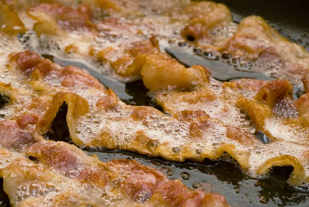 Closeup of bacon frying in a pan.