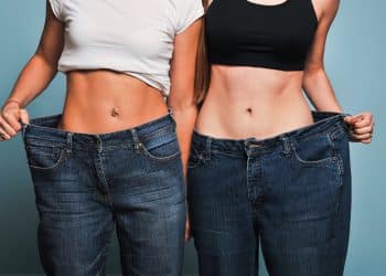 Two women standing by each other and pulling out their jeans to show how much skinnier they are than them.