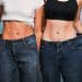 Two women standing by each other and pulling out their jeans to show how much skinnier they are than them.