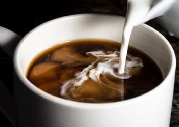 A closeup of some coffee creamer being poured into a cup of coffee.