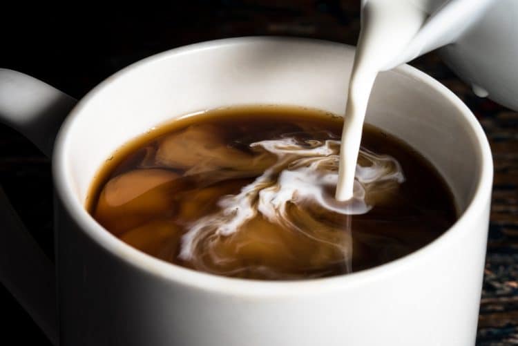 A closeup of some coffee creamer being poured into a cup of coffee.