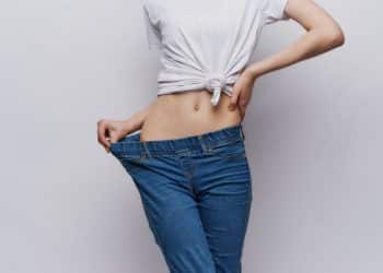 A woman only shown from her torso down to her legs, pulling her jeans out to show how much skinnier she is than them.
