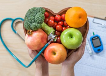 A closeup of a heart-shaped bowl of fruit, stethoscope, and diabetes monitor.