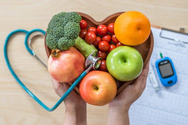 A closeup of a heart-shaped bowl of fruit, stethoscope, and diabetes monitor.